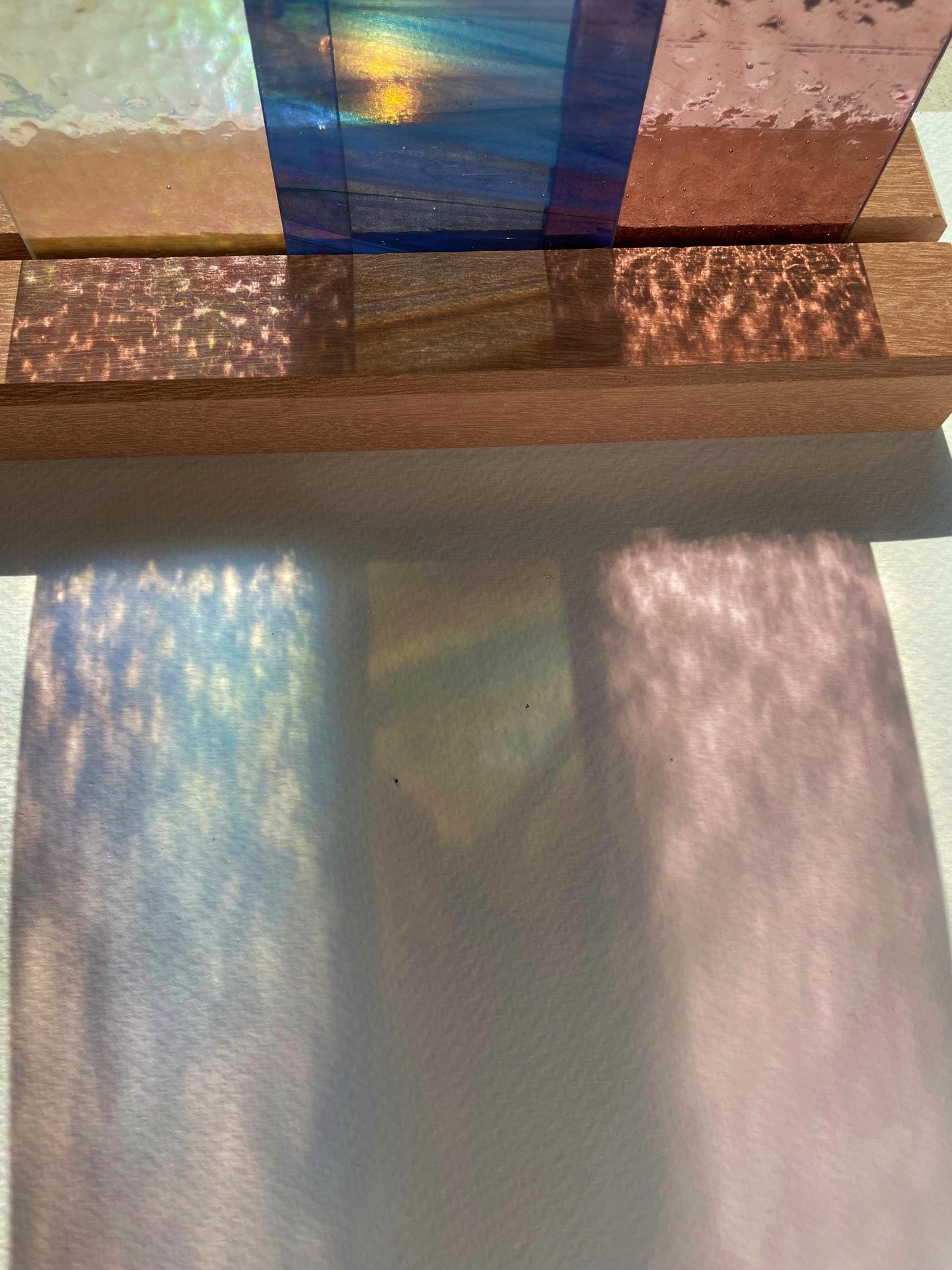 Eine Sammlung durchscheinender, farbiger Glasplatten auf einer Holzoberfläche, die bunte Schatten werfen. Die Muster ahmen die Textur und Farben des Glases nach und schaffen ein visuell ansprechendes Spiel aus Licht und Farbe